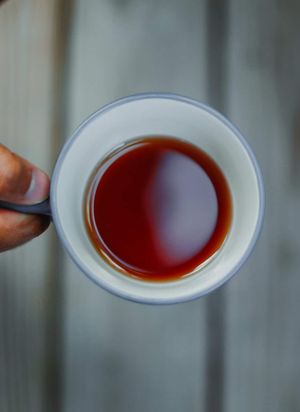 Hand holding a ceramic mug filled with dark coffee.