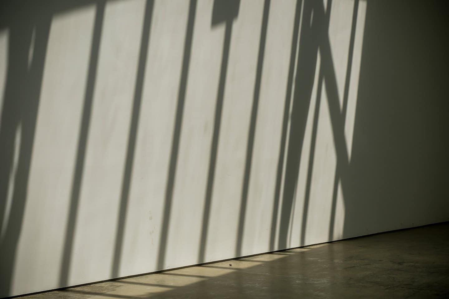 Abstract shadows create linear patterns on a wall and floor.