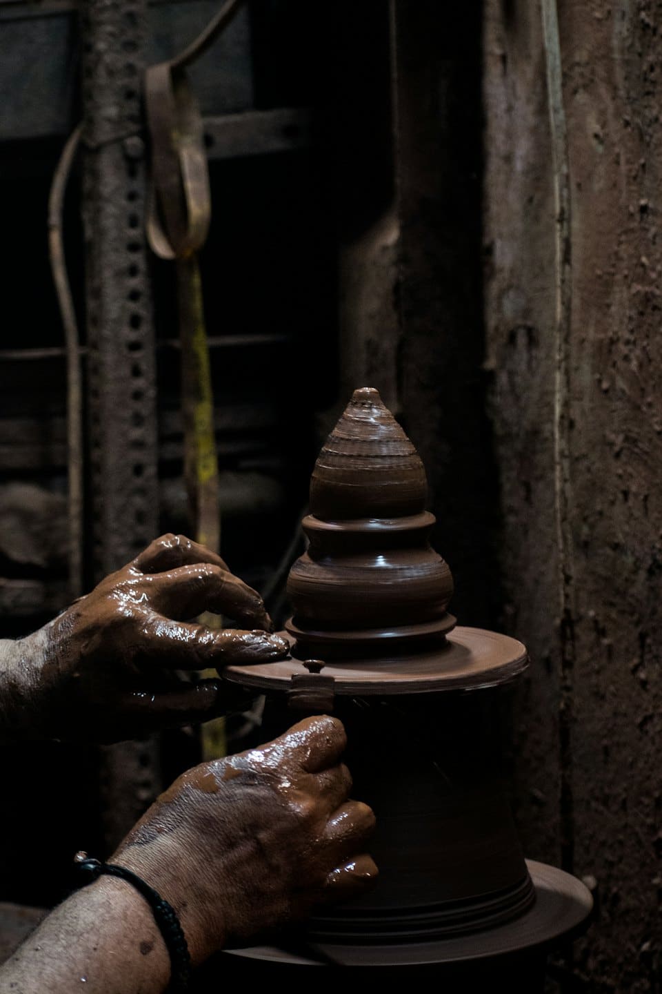 Potter shaping a wet clay vessel on a spinning wheel.