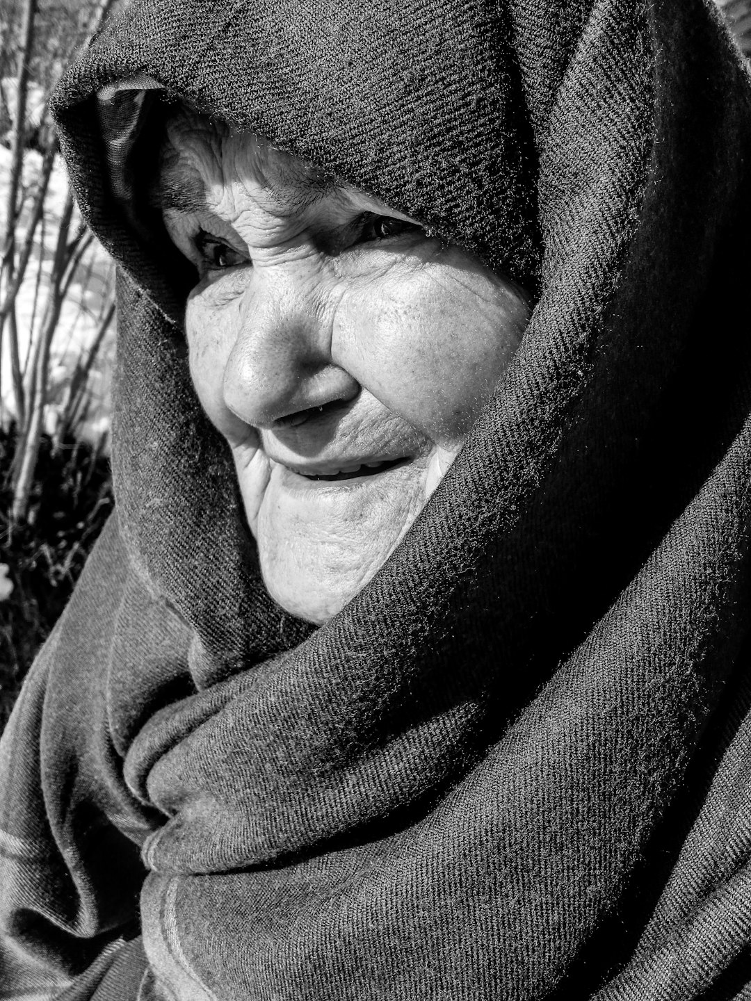 An elderly woman smiling while wearing a dark head covering.
