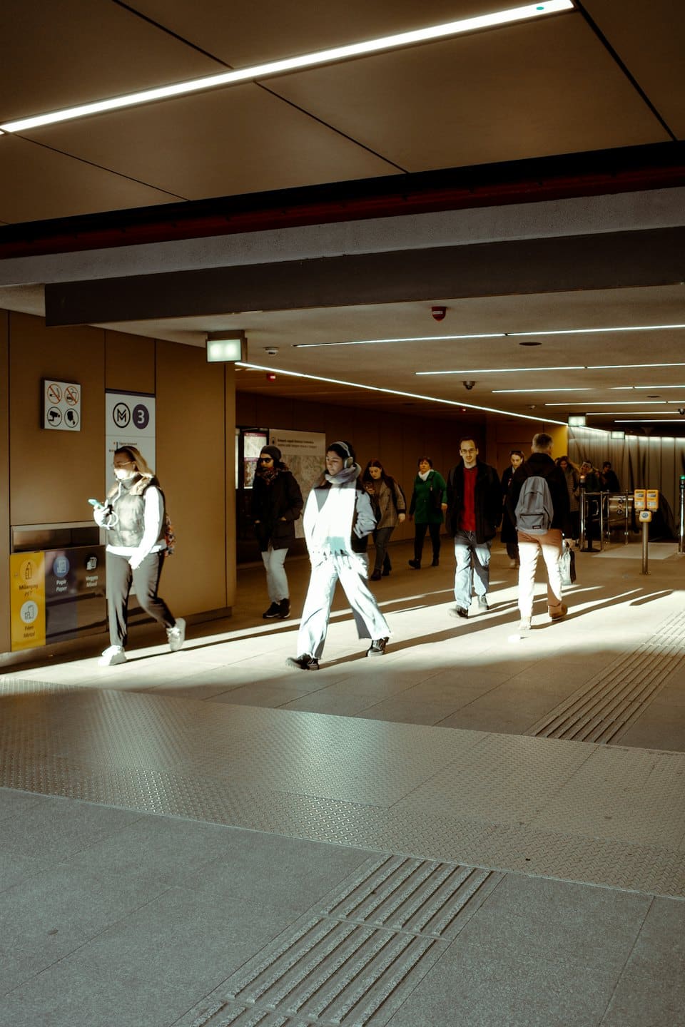 Commuters walk through a bright, modern subway station with tiled floors.