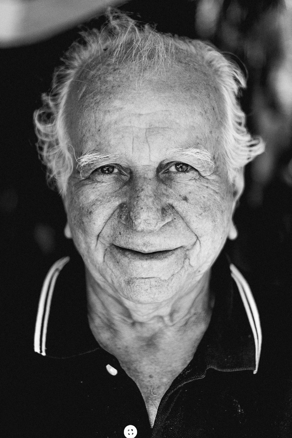 Elderly man with white hair smiles gently at the camera.