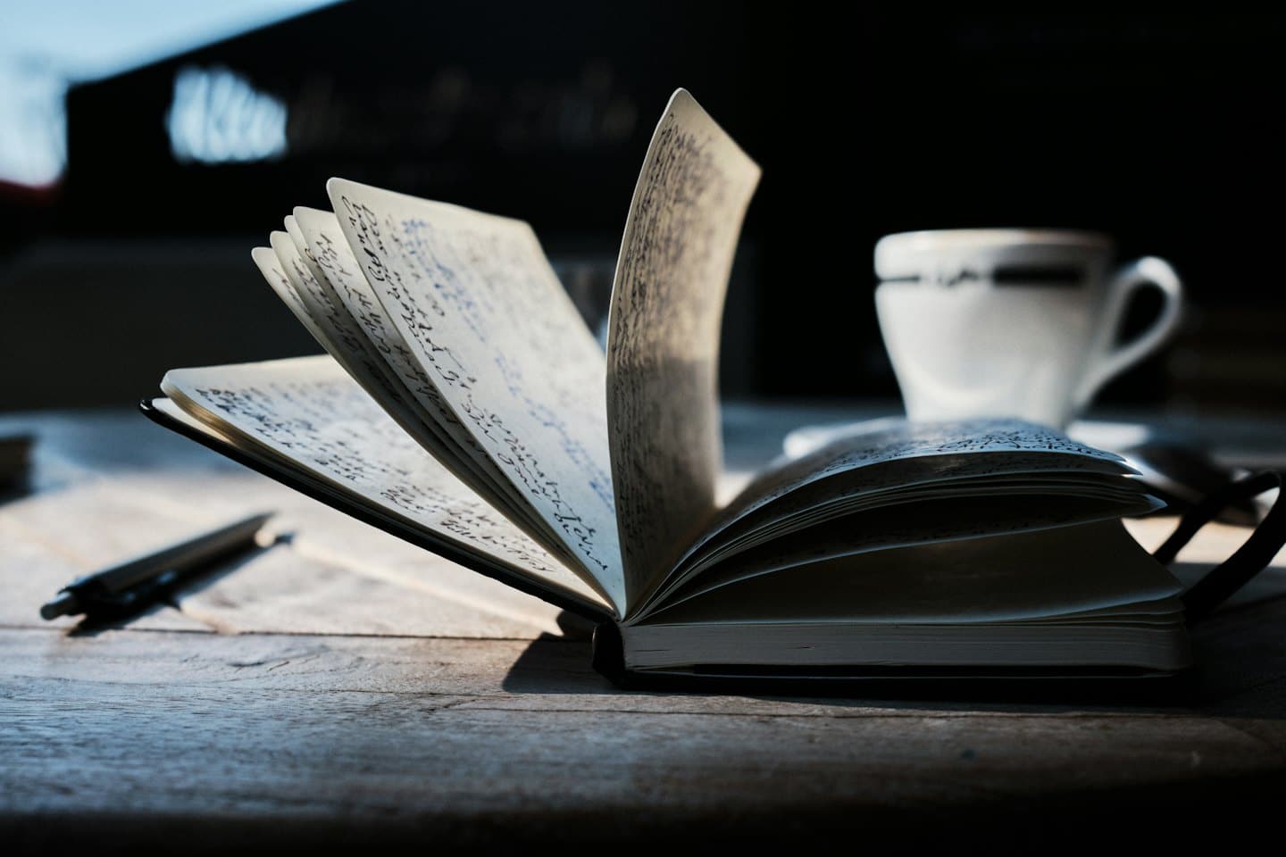 Notebook with illegible handwriting and a pen on a wooden table.